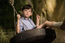 A young boy looks into the distance whilst swinging on a tyre