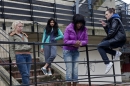 A group of teenage girls stand outside on some steps smoking