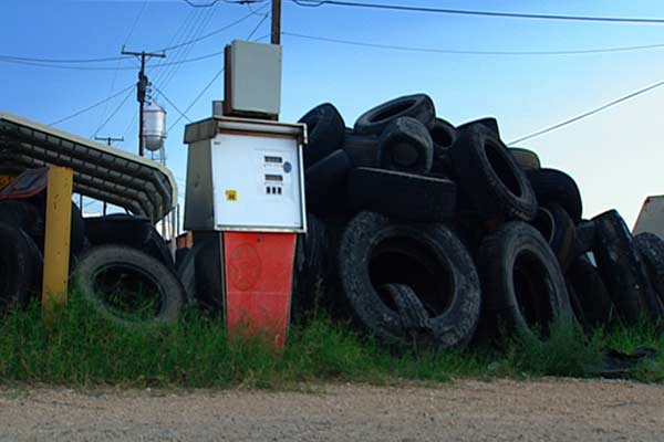 Still image from A Crude Awakening, of a disued petrol pump, next to a large pile of old tyres