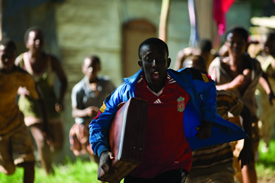 An African boy holds a suitcase under his arm as he runs away from village children who are chasing him.