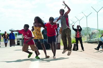 Four African children shout and jump at something happening out of the shot. 