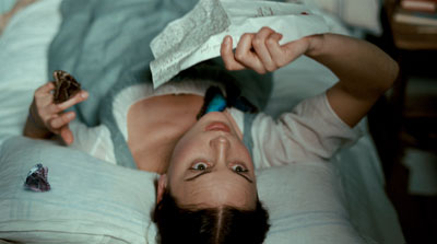High-angle shot of a young woman lying on a bed, a butterfly resting on one hand and an opened letter in the other