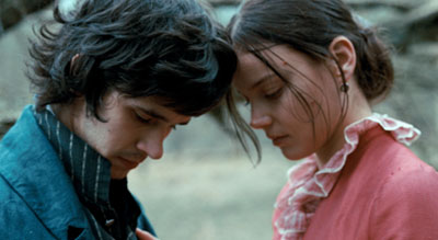 Medium close-up two-shot of a dark-haired young man and woman inclining their heads towards each other, their gazes cast down