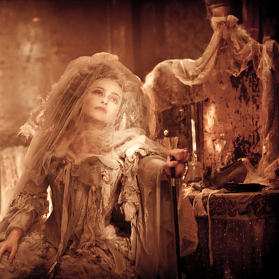 Mid-shot of a seated woman dressed in ragged bridal clothes in a dishevelled room