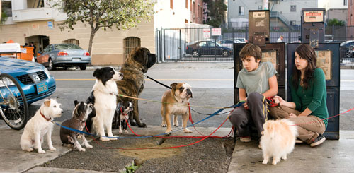 A still from the film of the two main characters hiding behind a post box holding on to the dogs leads