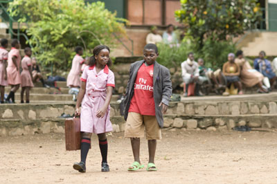 A girl in uniform and carrying a case walks next to a boy in an Arsenal t-shirt
