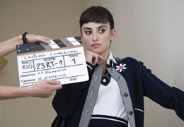 A dark haired female actor poses behind a pair of hands holding a clapperboard