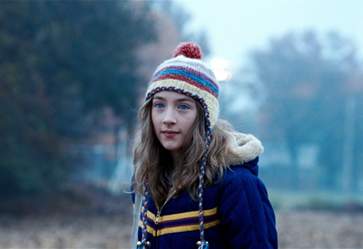 A medium shot of a teenage girl stood outside, wearing a wooly hat