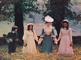 A woman holds the hands of two girls next to a boy walking through a meadow