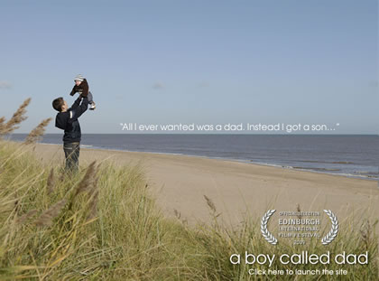 A young man holding a baby aloft on a beach