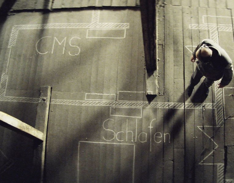 Still from the film, showing Captain Wiesler in a dusty attic room, stood ecaming the plan of Dreyman's apartment, which is drawn in chalk on the bare floorboards