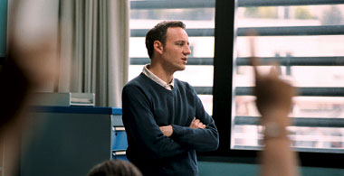 Teacher François stands with crossed arms at the front of The Class, framed by his students' raised hands