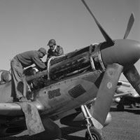 Two African-American flight engineers work on the engine of a plane